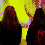 Duas mulheres observam uma obra de arte digital colorida em uma galeria de museu.