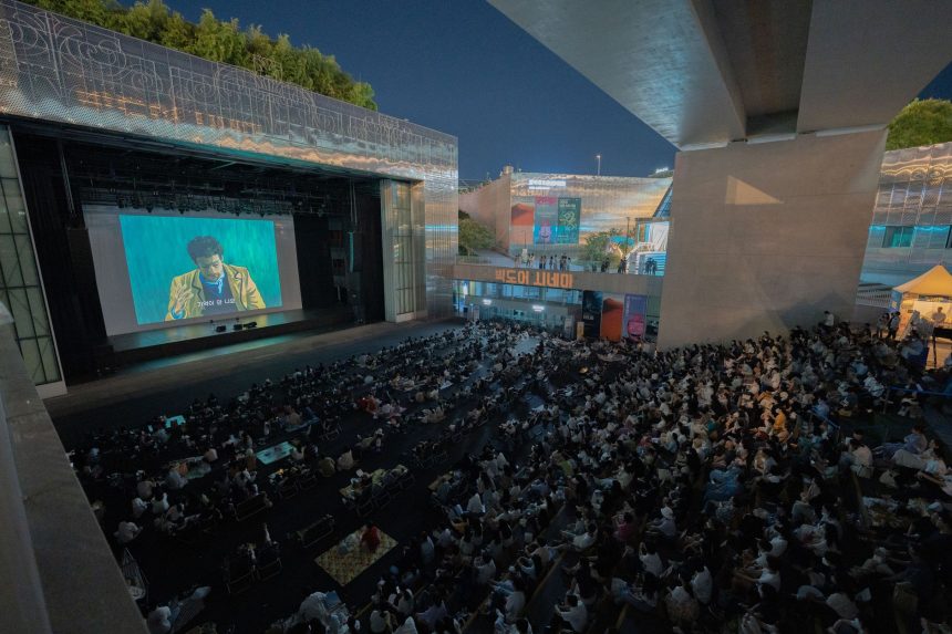 Público assiste a uma sessão de cinema ao ar livre durante a noite, sob um viaduto.